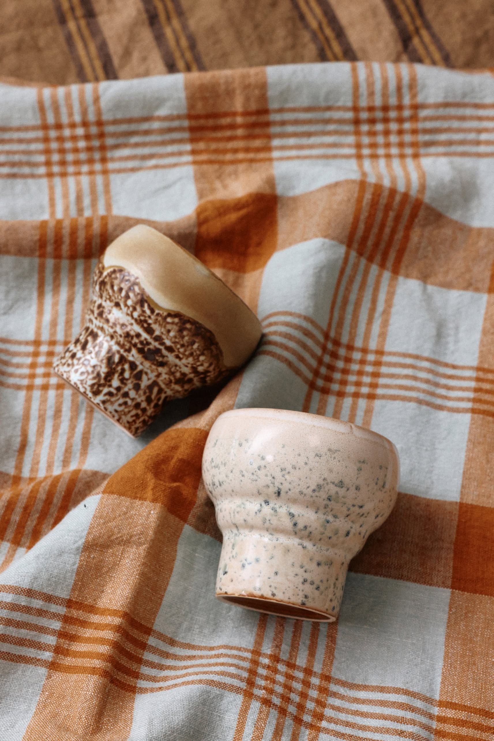 Two small ceramic cups rest on HKLIVING Vida Check Tea Towel in Amber/Blue, adding charm and function to your space.