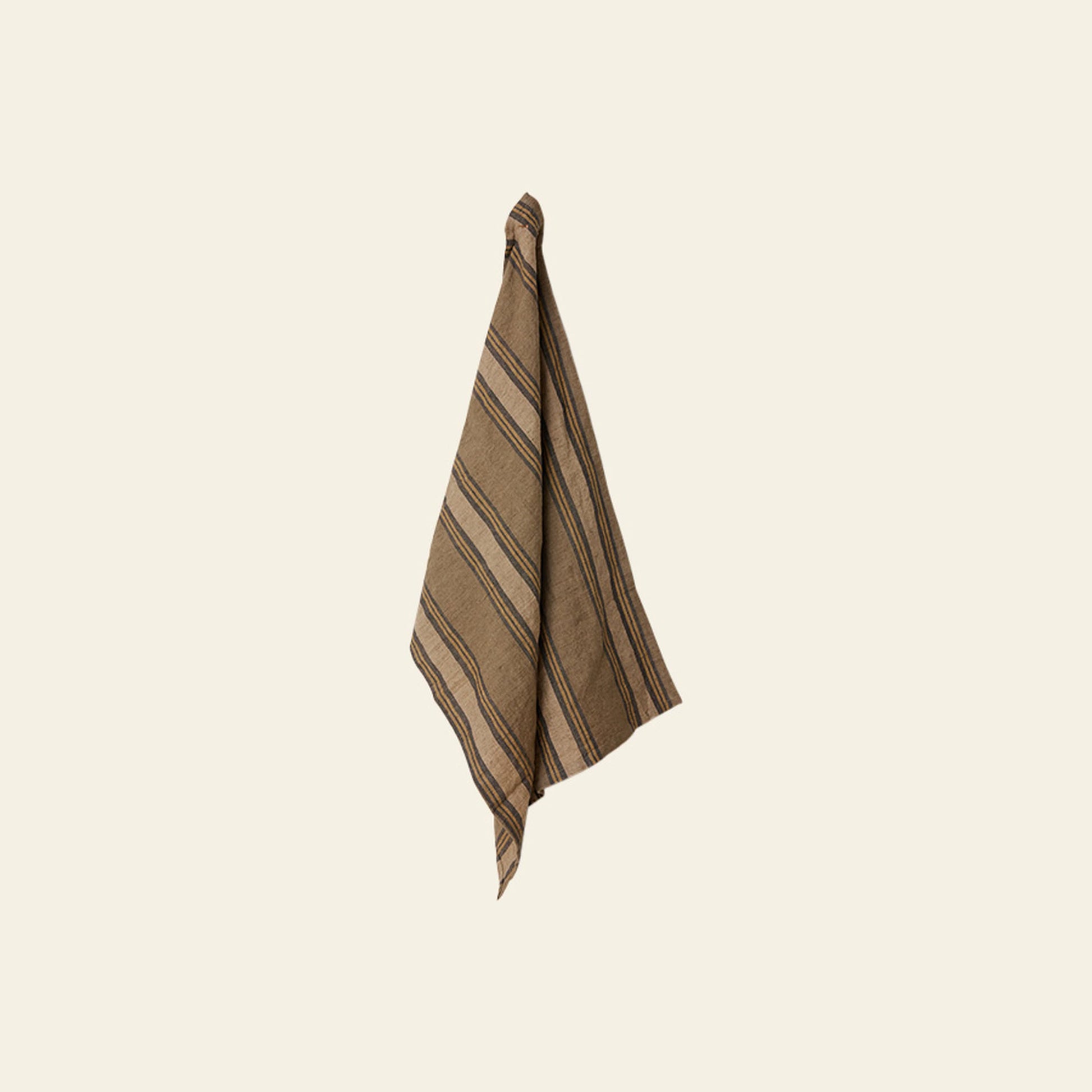 The HKLIVING Vida Striped Tea Towel in Sand/Cream, featuring a simple blend of diagonal sand and cream stripes, hangs on a light beige wall—its linen and cotton textures create a classic look.