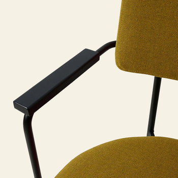 Close-up of the HKLIVING Dining Armchair in Main Line Flax mustard yellow fabric, featuring black metal armrests and frame. A modern Dutch-inspired design by HKLIVING, shown against a plain light background.