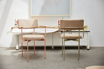 Two HKLIVING Dining Armchairs, Main Line Flax, Nude—with metal frames and beige cushions—are arranged by a white desk in a bright, minimalist room.