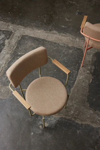 A top-down view of two modern HKLIVING Dining Armchairs with round brown seats, curved backrests, and wooden armrests on a dark textured floor. One frame is olive (HKLIVING Main Line Flax), the other peach.