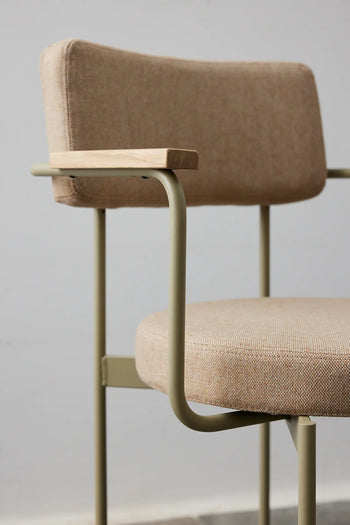 The HKLIVING Dining Armchair, Main Line Flax in Olive, features a metal frame, light wooden armrests, and an upholstered seat and backrest—an elegant example of Dutch design set against a plain light gray background.