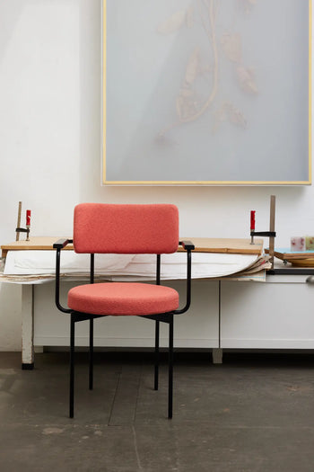An HKLIVING Dining Armchair, Yoredale in black, with black metal legs and armrests, is placed before a white workbench. Above hangs a pale artwork, while two clamps grip the bench—an elegant touch of Dutch design from HKLIVING.