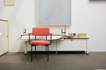 An HKLIVING Dining Armchair, Yoredale, Black with plush cushioning and black metal legs is centered in front of a white desk in a minimalist room with Dutch design, white walls, and displayed art.