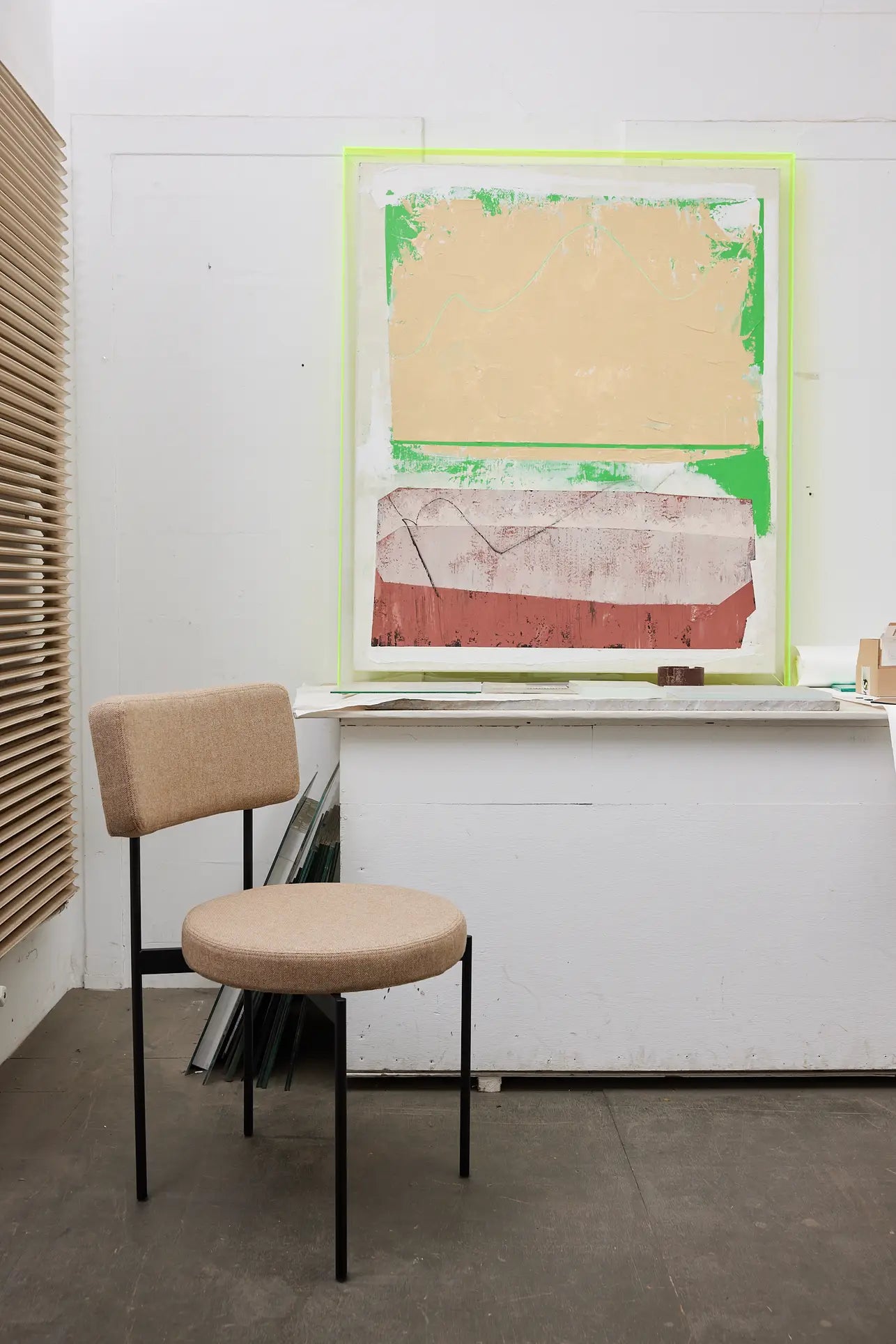 A HKLIVING Dining Chair, Main Line Flax, Black, stands before a white table. On the wall behind, an abstract artwork in tan, green, and red blocks adds color to this modern studio space.