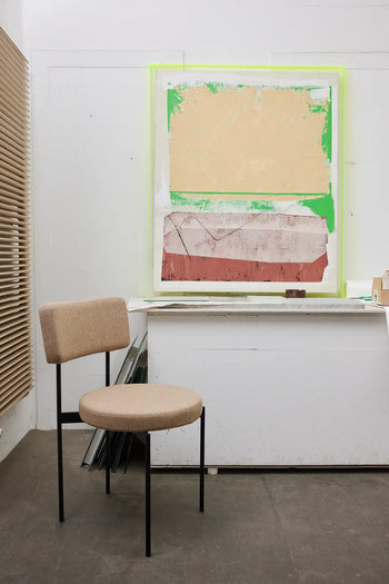 A HKLIVING Dining Chair, Main Line Flax, Black, stands before a white table. On the wall behind, an abstract artwork in tan, green, and red blocks adds color to this modern studio space.