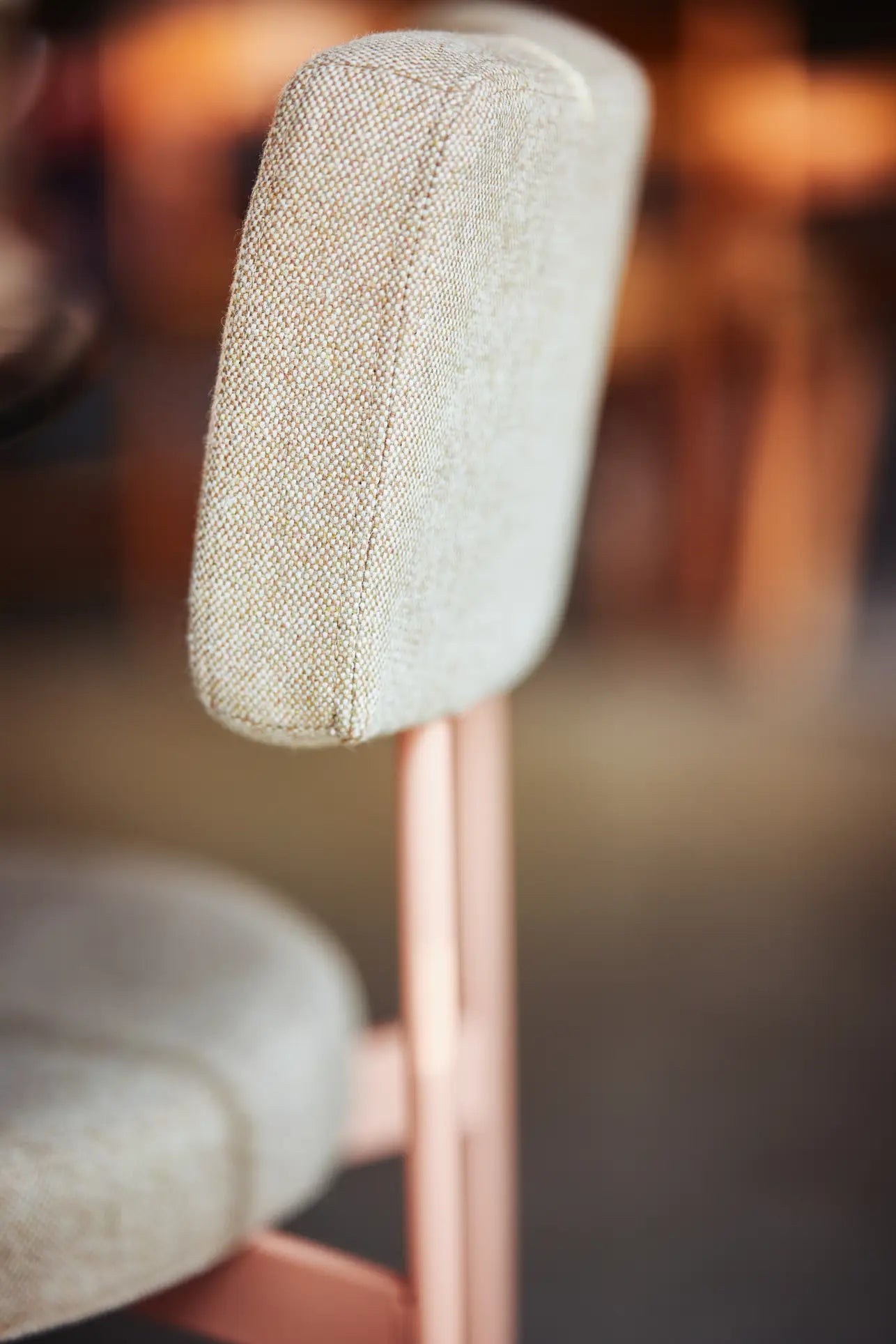 A close-up of the HKLIVING Dining Chair, Main Line Flax in Nude, featuring a light beige upholstered backrest and seat on a light pink metal frame, with a blurred background.
