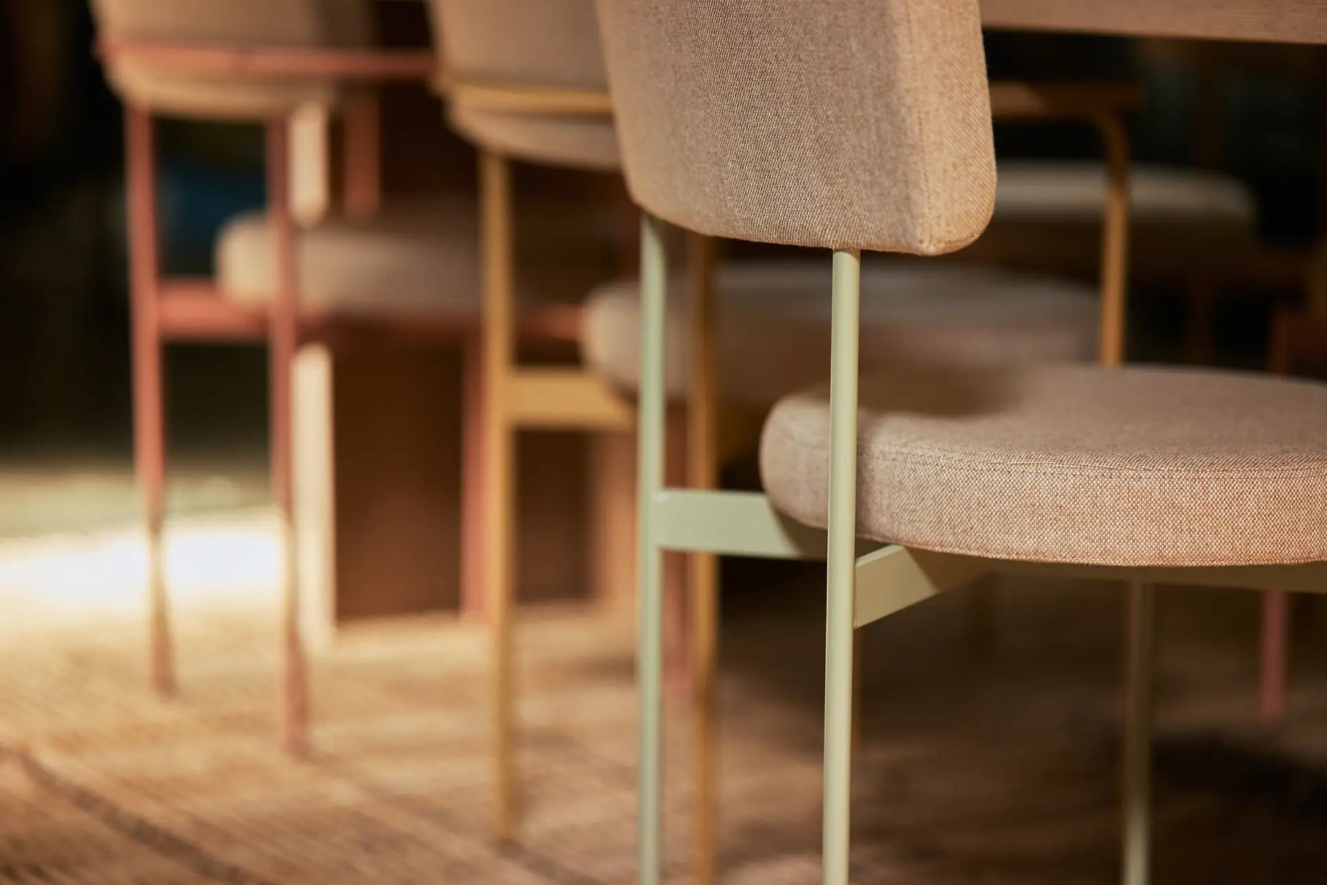 Close-up of HKLIVING Dining Chair, Main Line Flax in Olive, featuring metal legs and arranged around a wooden table on a patterned rug in a warmly lit room.
