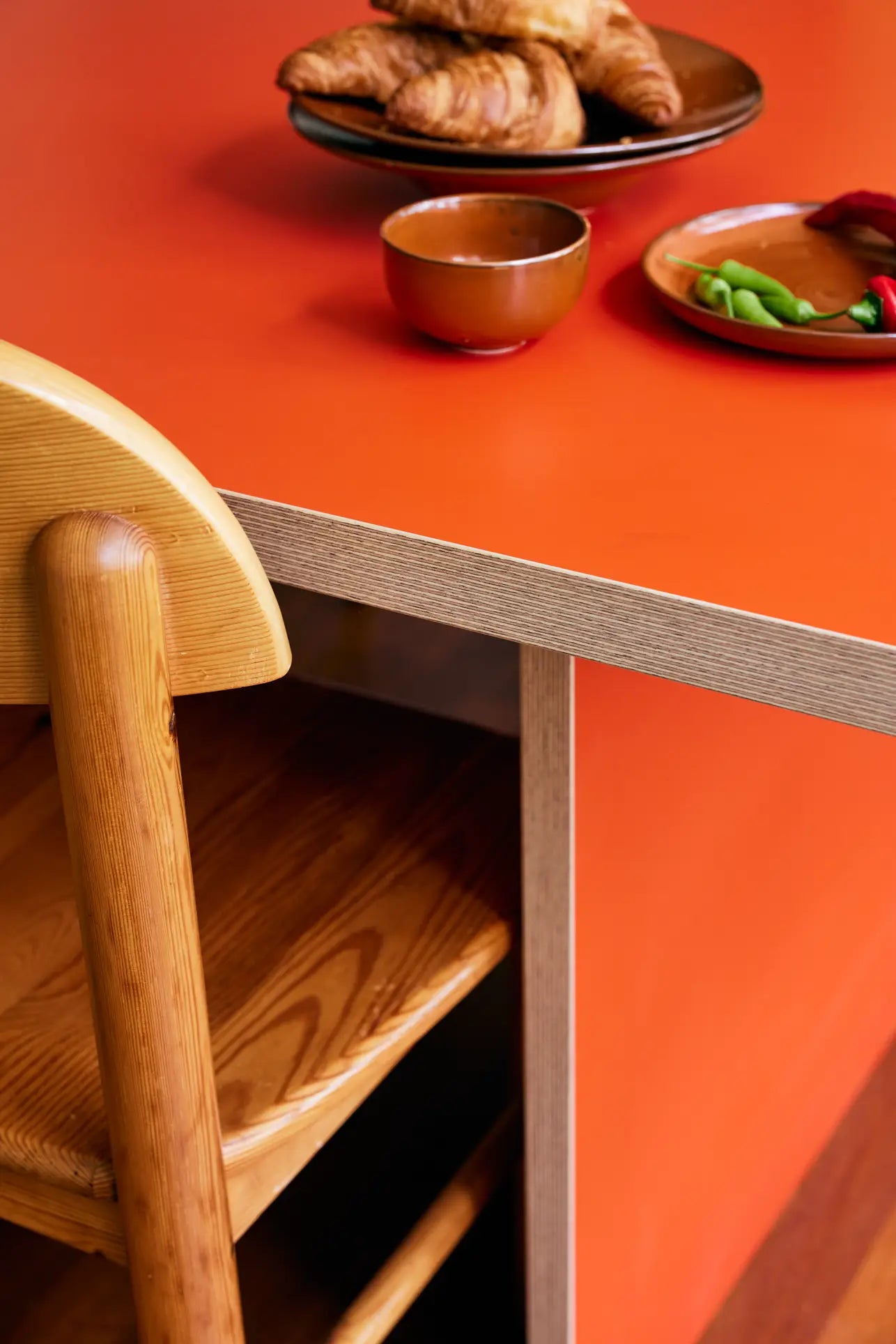 A wooden chair is tucked under the HKLIVING Rectangular Dining Table (220cm), which has pastries, a brown bowl, and a small plate with green beans and a red chili on top.
