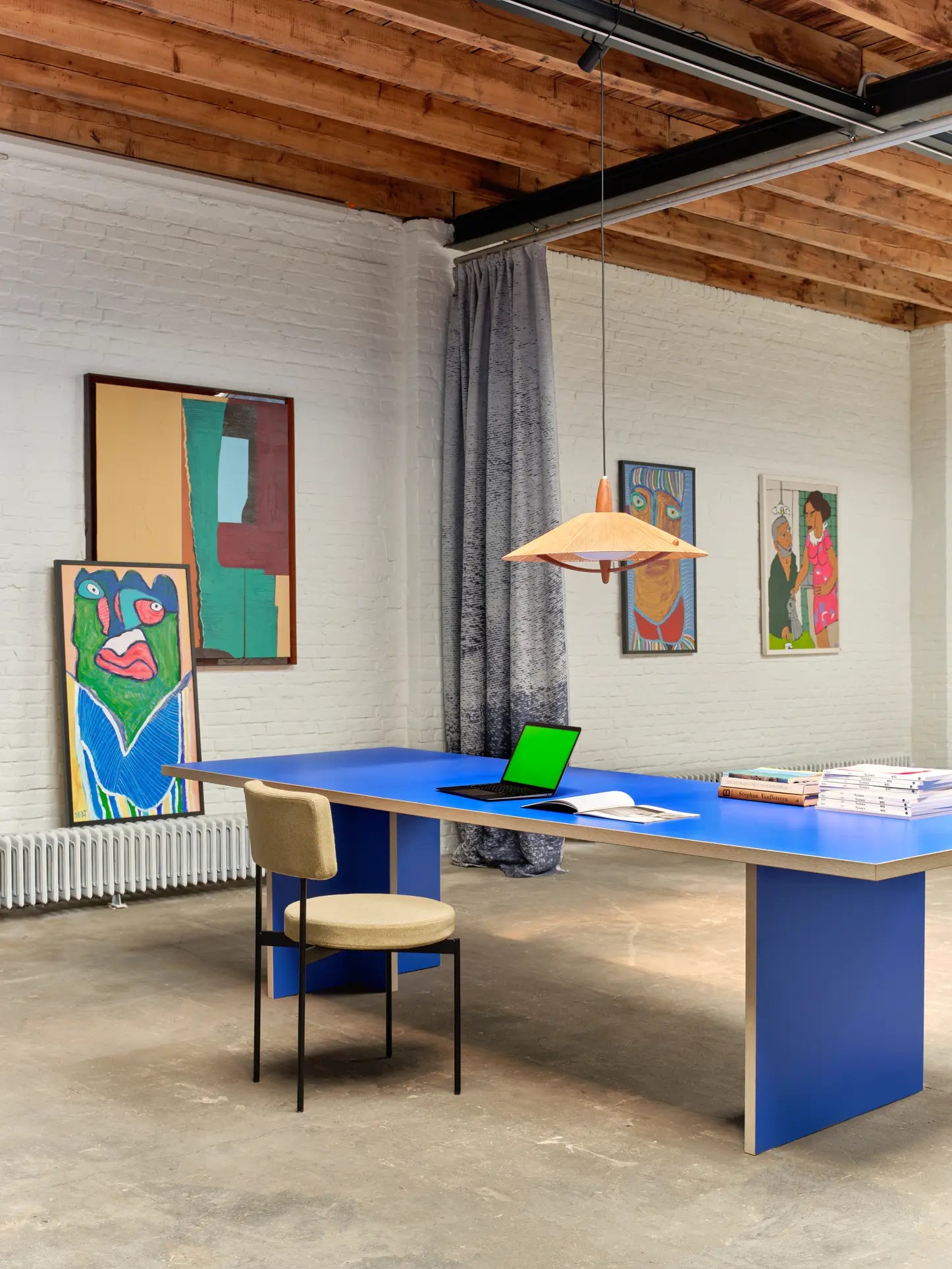 A creative workspace features the HKLIVING Dining Table (280cm, Rectangular) by HKLIVING as a vibrant centerpiece, with abstract art on white brick walls and exposed wooden beams completing the stylish, timeless design.