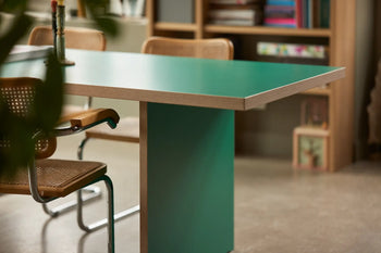 A HKLIVING Dining Table, Rectangular, 280cm with wooden edges is paired with cane and metal chairs. Behind it, a bookshelf holds books and decor, giving the modern space a cozy feel with timeless design elements.