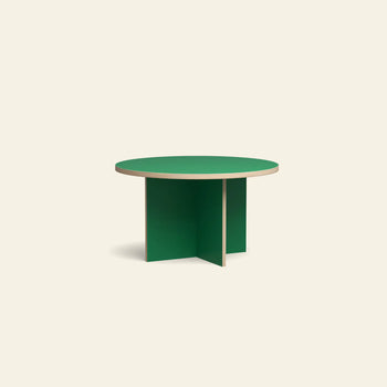 The HKLIVING Dining Table, Round, 130cm features a green top with a light wood edge and a base of two intersecting green panels, shown against a beige background.