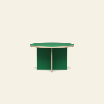 The HKLIVING Dining Table, Round, 130cm by HKLIVING features a minimalist design with a light wood edge and intersecting green panel legs, shown against a plain off-white background.