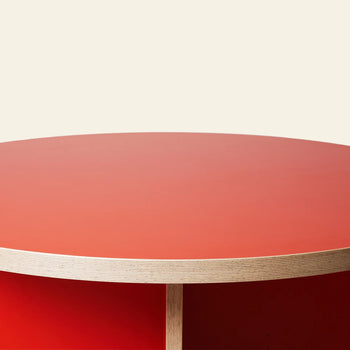 A close-up of the HKLIVING Dining Table, Round, 130cm, featuring a red top and exposed plywood edge by HKLIVING, displayed against a plain light background.