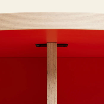 Close-up of the HKLIVING Dining Table, Round, 130cm, showing its light wood tabletop and red underside with a focus on the connection to the vertical wooden support—a stylish centerpiece for contemporary dining rooms.