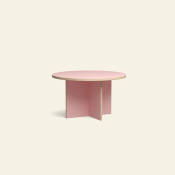 A round coffee table with a light wood top and light pink cross-shaped base, inspired by the HKLIVING Dining Table, Round, 130cm, from HKLIVING, set against a plain off-white background.