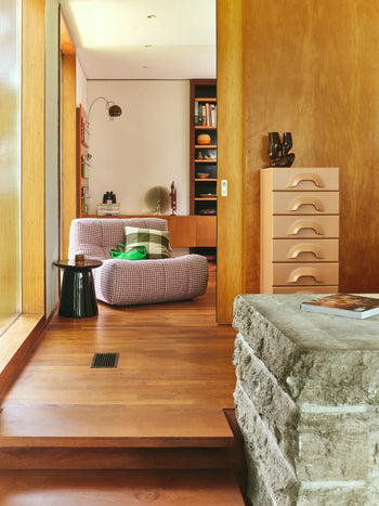 A cozy, modern interior with wood floors and walls, a stone step, the HKLIVING Lazy Lounge Chair in playful prints, a black side table, a peach drawer unit, and built-in shelves in the background.