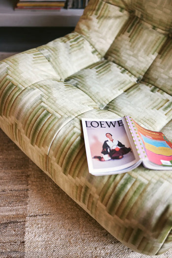 A magazine and a colorful notebook sit on an HKLIVING Lazy Lounge Chair, with part of a textured beige rug visible on the nearby floor.