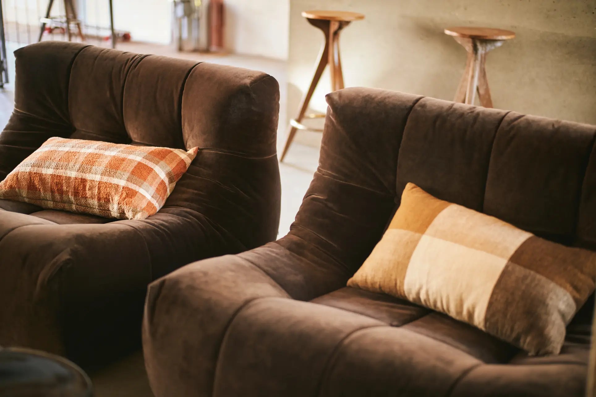 Two HKLIVING Lazy Lounge Chairs with soft, plaid cushions are arranged in a cozy room. Wooden stools in the background against a neutral wall add warmth and invite relaxation to the space.
