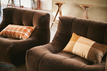 Two HKLIVING Lazy Lounge Chairs with soft, plaid cushions are arranged in a cozy room. Wooden stools in the background against a neutral wall add warmth and invite relaxation to the space.