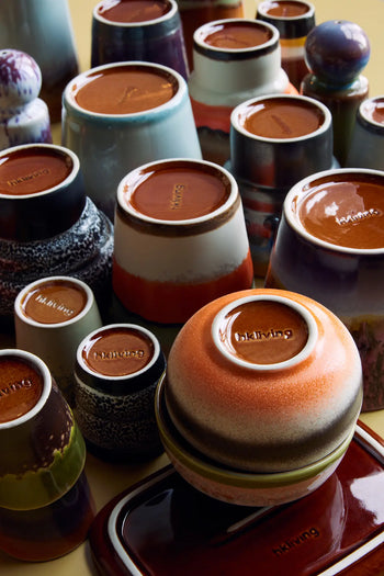 Several colorful HKLIVING 70s Ceramics Cappuccino Mugs are shown upside down, displaying the HKLIVING brand name. The set features varied glazes, patterns, and sizes.
