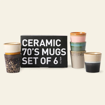 A set of six HKLIVING 70s Ceramics coffee mugs is shown in front of a branded box. Each mug features unique handcrafted glazing inspired by the vibrant patterns and hues of classic 70s ceramics.