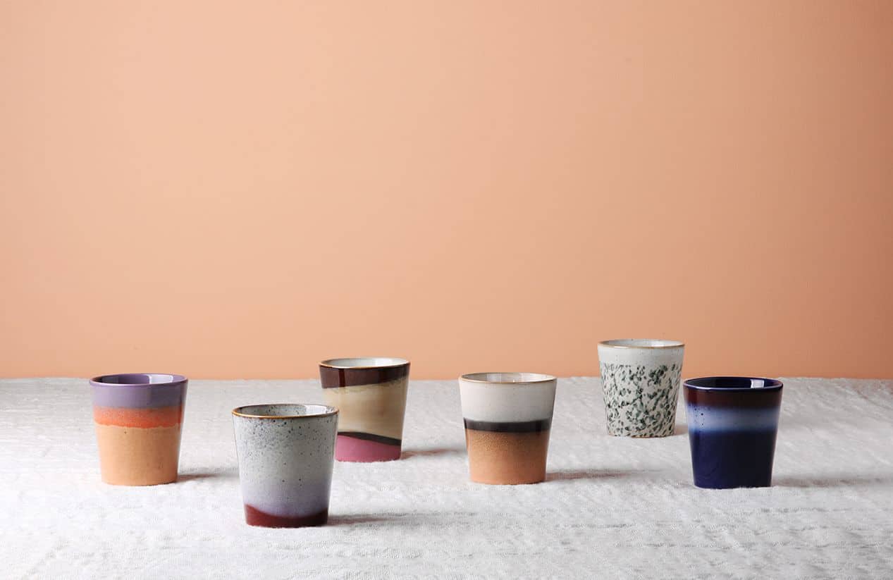 The HKLIVING 70s Ceramics: Coffee Mugs, Set of 6, features handcrafted glazed designs in assorted patterns and colors, arranged on a textured white surface against a plain peach background.