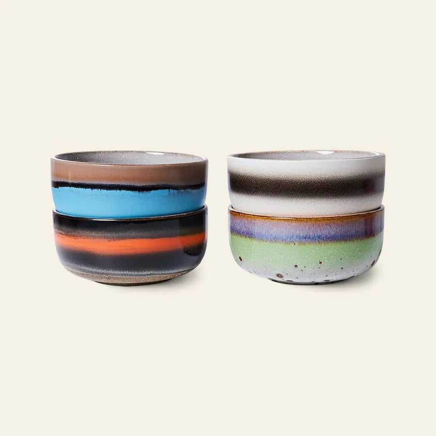 The HKLIVING 70s Ceramics Dessert Bowls, Set of 4, feature retro stripes in blue, orange, green, and purple. These earthy-toned bowls from HKLIVING stand out with their vintage design against a simple beige background.