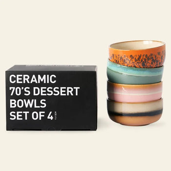 A black box labeled "HKLIVING 70s Ceramics: Dessert Bowls, Set of 4" sits beside a stack of vibrant HKLIVING dessert bowls, each showcasing retro patterns and earthy tones inspired by classic 70s ceramic designs.