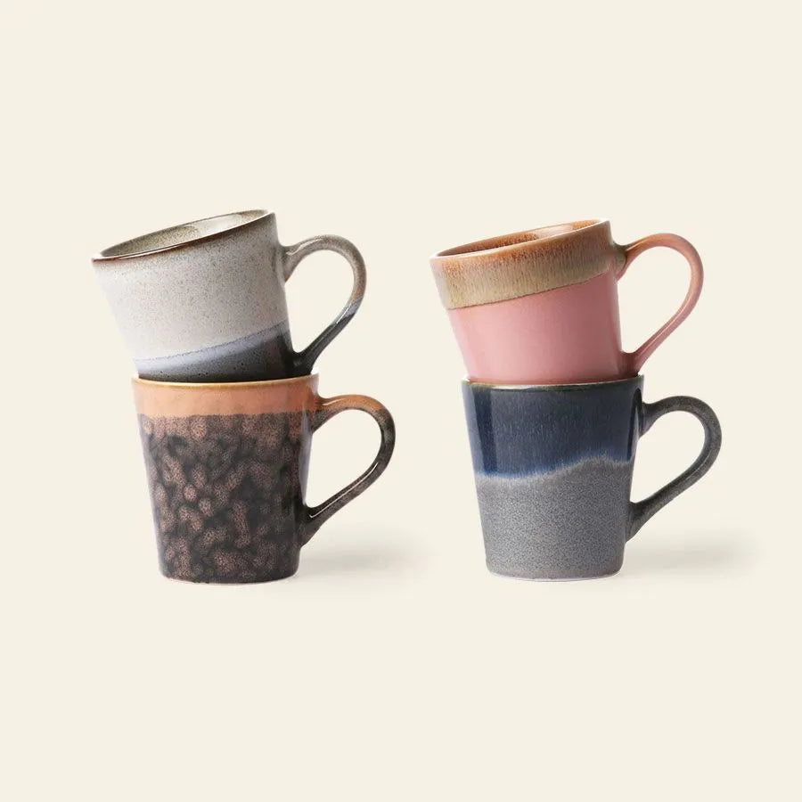 The HKLIVING 70s Ceramics Espresso Mugs Set of 4 features mugs in earth tones and pastels, each with a unique handcrafted color pattern and texture, stacked in two uneven piles against a plain light background.