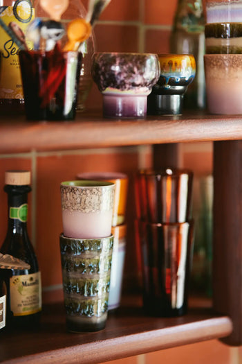 HKLIVING 70s Ceramics Latte Mugs (Set of 2) by HKLIVING are displayed on wooden shelves against a reddish-tiled wall, showcasing handcrafted glaze and unique textures for a vibrant, eclectic look.