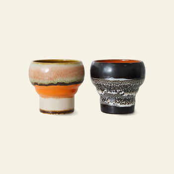 HKLIVING 70s Ceramics: Lungo Mugs, Set of 2, feature retro designs—one with brown, pink, cream, and orange bands; the other in black with white and gray patterns—resting on a light beige background. Both mugs are by HKLIVING.
