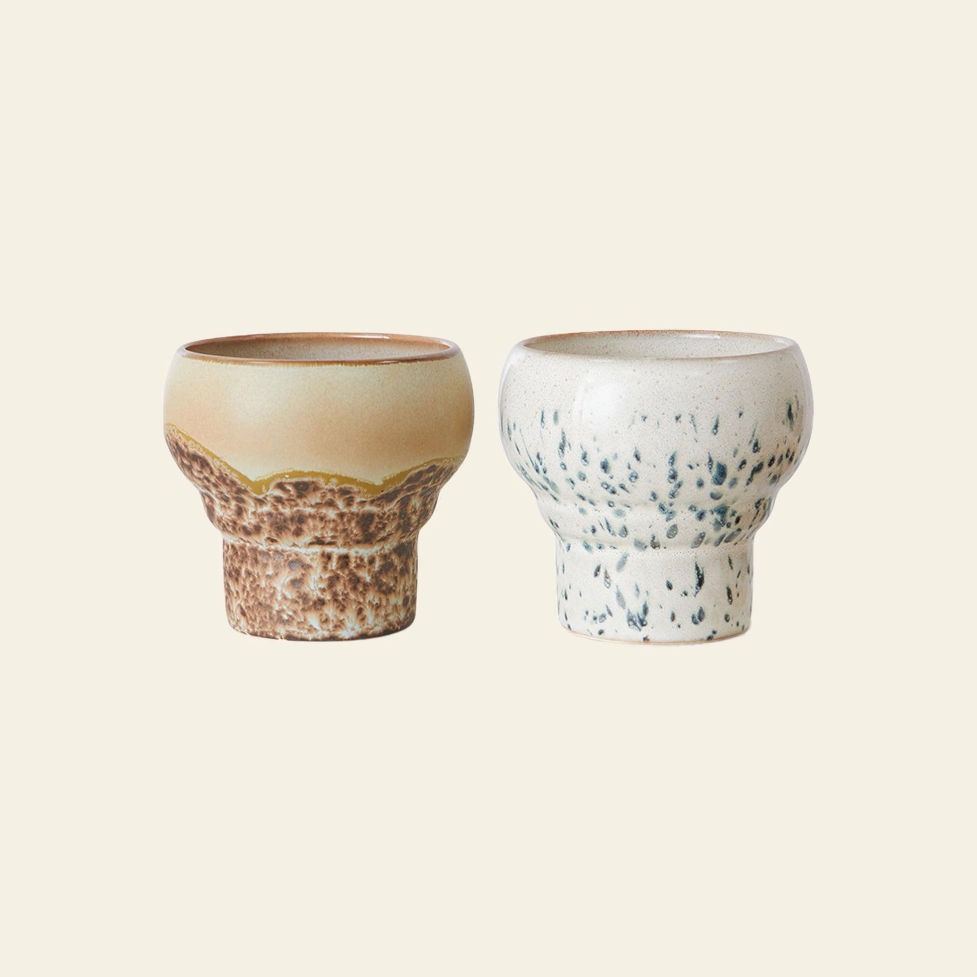 The HKLIVING 70s Ceramics: Lungo Mugs, Set of 2 features one brown mug with texture and one off-white mug with green speckles, both on a cream background. Perfect retro mugs from HKLIVING.