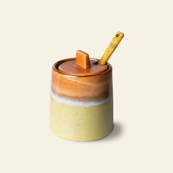The HKLIVING 70s Ceramics Sugar Pot, part of the Milk Jug & Sugar Pot set, features a lid, wooden spoon, and a classic 70s-inspired gradient design in light beige, white, and brown against a light background.