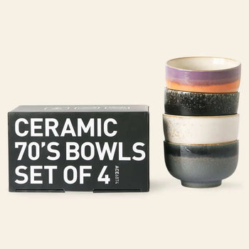 A black box labeled HKLIVING 70s Ceramics: Noodle Bowls, Set of 4 is placed beside a stack of colorful HKLIVING stoneware bowls, each with a unique 70s-inspired design, on a plain light background.