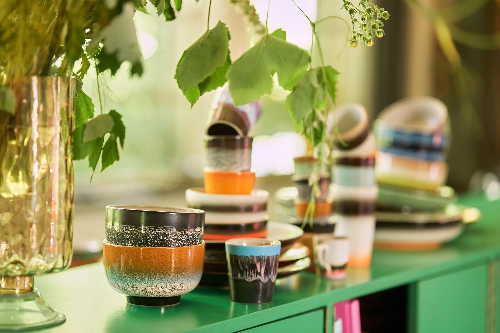 A set of HKLIVING 70s Ceramics Noodle Bowls is stacked on a bright green surface, with leafy plants hanging above and sunlight streaming through a window in the background.