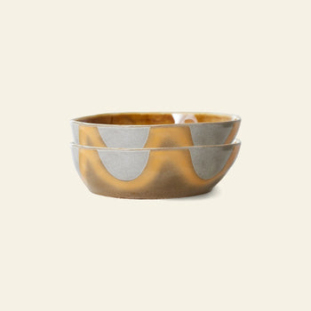 Two stacked HKliving 70s Ceramics Pasta Bowls, Set of 2, display a wavy abstract pattern in matte gray and glossy ochre brown—ideal for an elegant table setting on a light beige background.