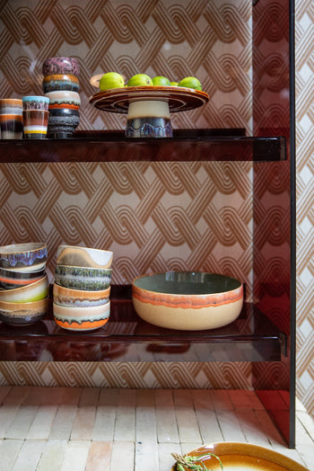 HKLIVING 70s Ceramics Salad Bowls by HKLIVING, with retro earthy patterns, are displayed on shelves—some holding green apples—set against a geometric beige and orange retro-style wallpaper.