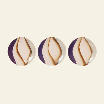 Two HKLIVING 70s Ceramics side plates, featuring a white and brown swirl pattern, are displayed in a row on a plain light beige surface against a purple background.