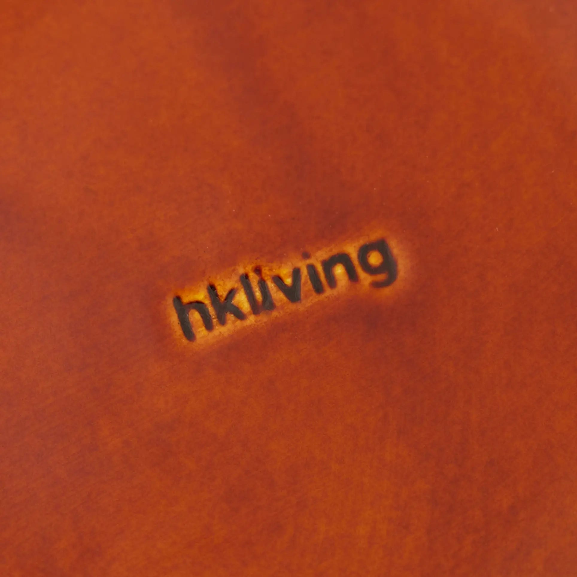 Close-up of a brown leather surface stamped with the HKLIVING logo, echoing the textured charm and retro appeal of the HKLIVING 70s Ceramics: Side Plates, Set of 2. Subtle, darkened, and deeply indented for a vintage look.