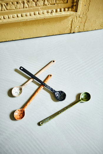 The HKLIVING 70s Ceramics: Spoons L, Set of 4 features black, gold, copper, and silver spoons arranged on a textured surface near a decorative gold frame, capturing the retro charm of the 70s.