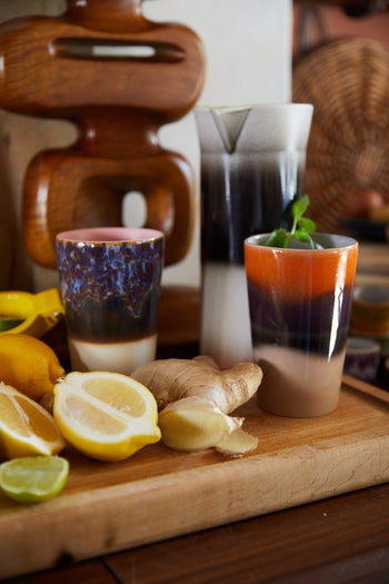 HKLIVING 70s Ceramics Tea Mugs, Set of 2, rest on a wooden board with lemons, lime, ginger, and mint. Abstract wood decor and a woven basket from the brand are softly blurred in the background.