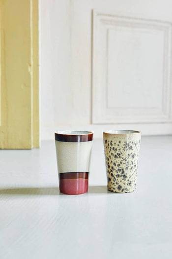 Two HKliving 70s Ceramics Tea Mugs sit on a light surface—one features cream, brown, and rust-red bands for a vintage look, while the other is beige with a mottled brown speckle. Pale walls enhance the retro 70s Ceramics vibe.