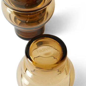 Four rounded amber HKLIVING 70s Glassware Bulb Glasses rest on a white surface, each casting soft shadows. The HKLIVING logo appears on the rim of one glass, evoking the retro charm of 1970s design.