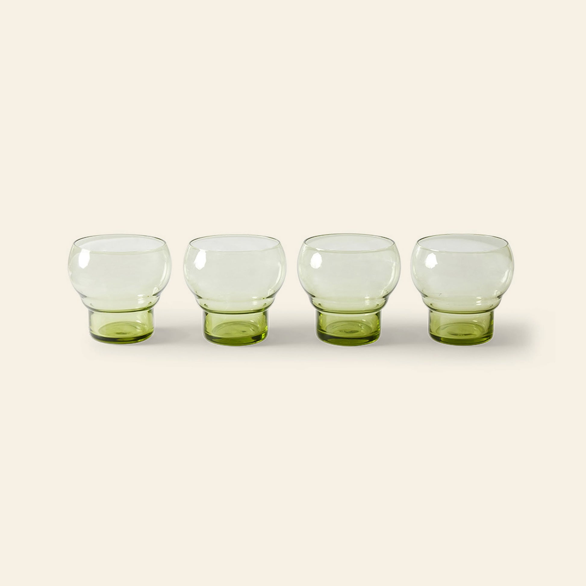 The HKLIVING 70s Glassware: Bulb Glasses, Set of 4, features four short, round clear cups with green-tinted bases arranged in a row on a light beige background.