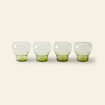 The HKLIVING 70s Glassware: Bulb Glasses, Set of 4, features four short, round clear cups with green-tinted bases arranged in a row on a light beige background.