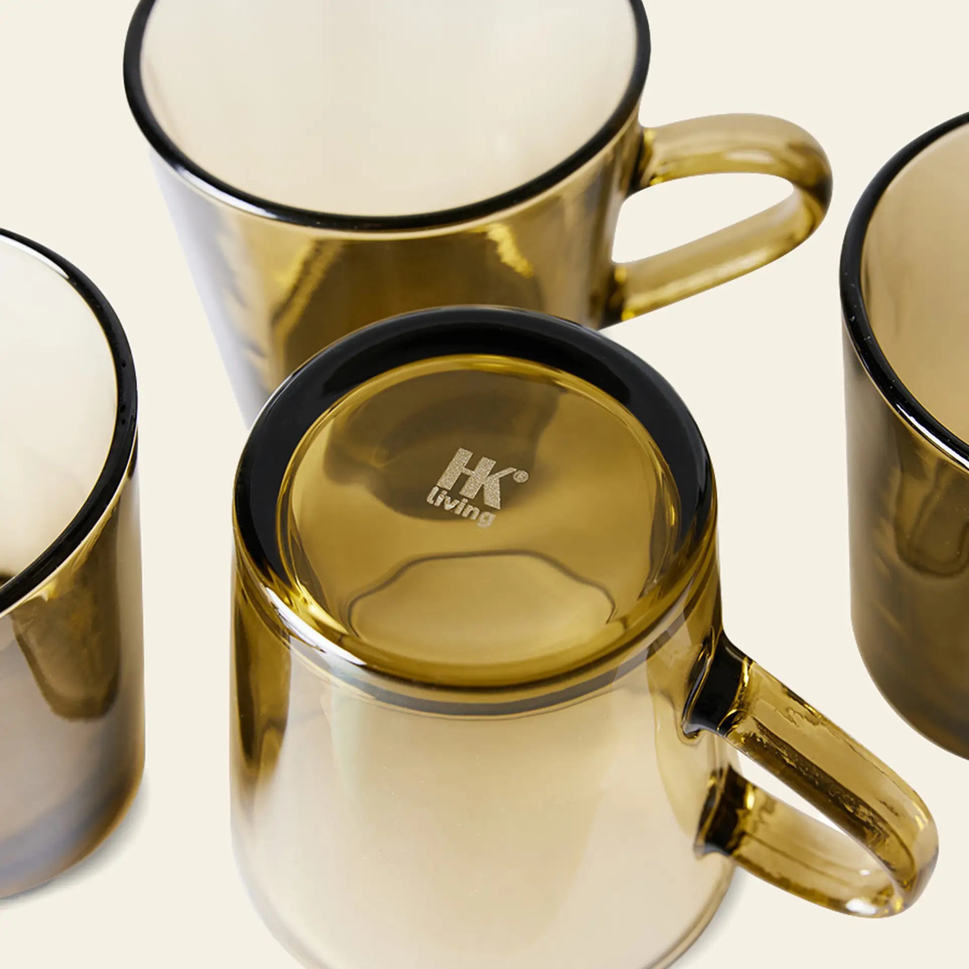 Four HKLIVING 70s Glassware Coffee Cups are arranged on a light surface; three stand upright, while one is upside down, revealing the HKLIVING logo—a vibrant homage to retro style.