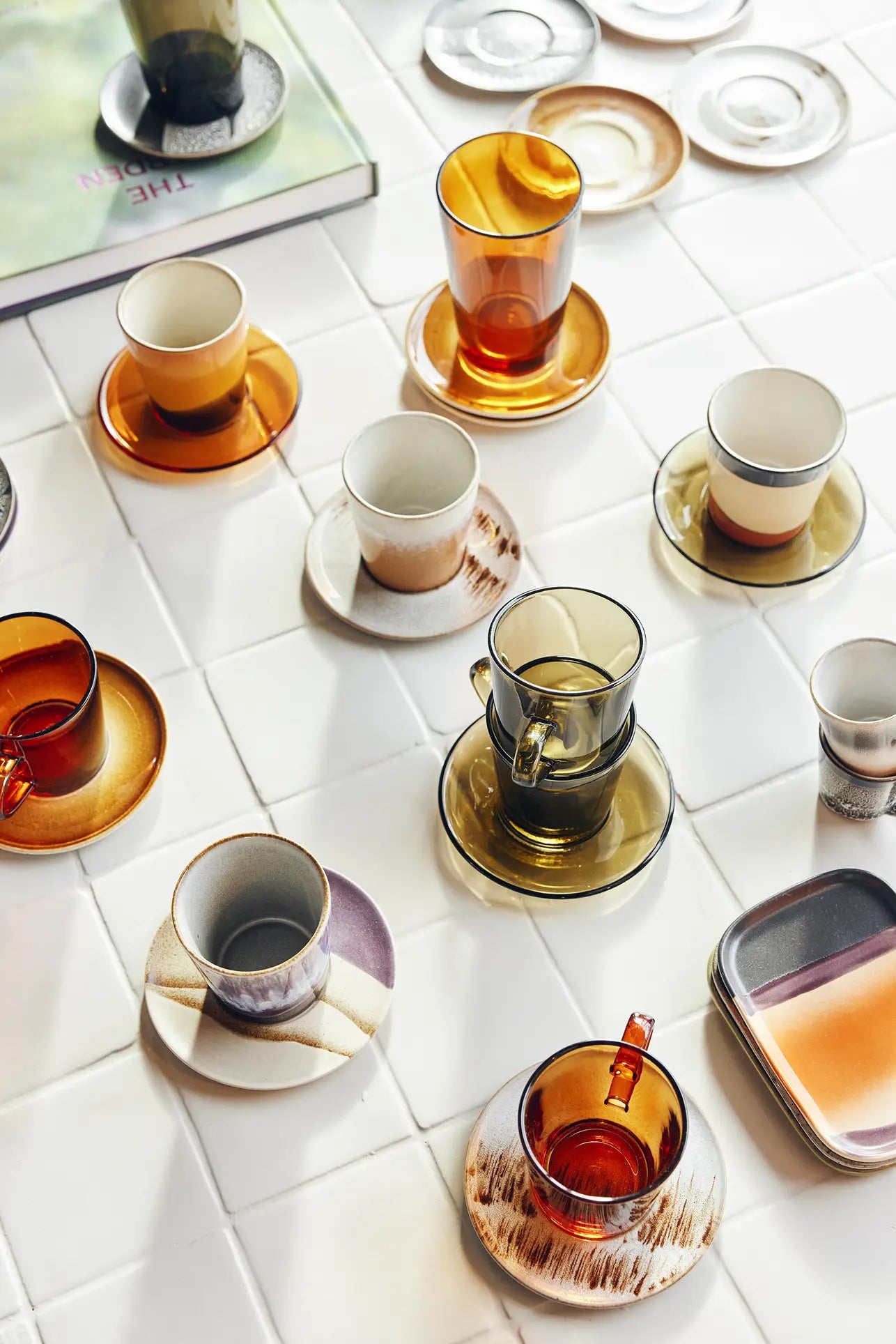 HKLIVING 70s Glassware: Coffee Cups, Set of 4, inspired by earthy 70s style, are displayed with ceramic saucers on white tiles next to a book and two rectangular plates.