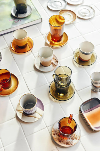 HKLIVING 70s Glassware: Coffee Cups, Set of 4, inspired by earthy 70s style, are displayed with ceramic saucers on white tiles next to a book and two rectangular plates.