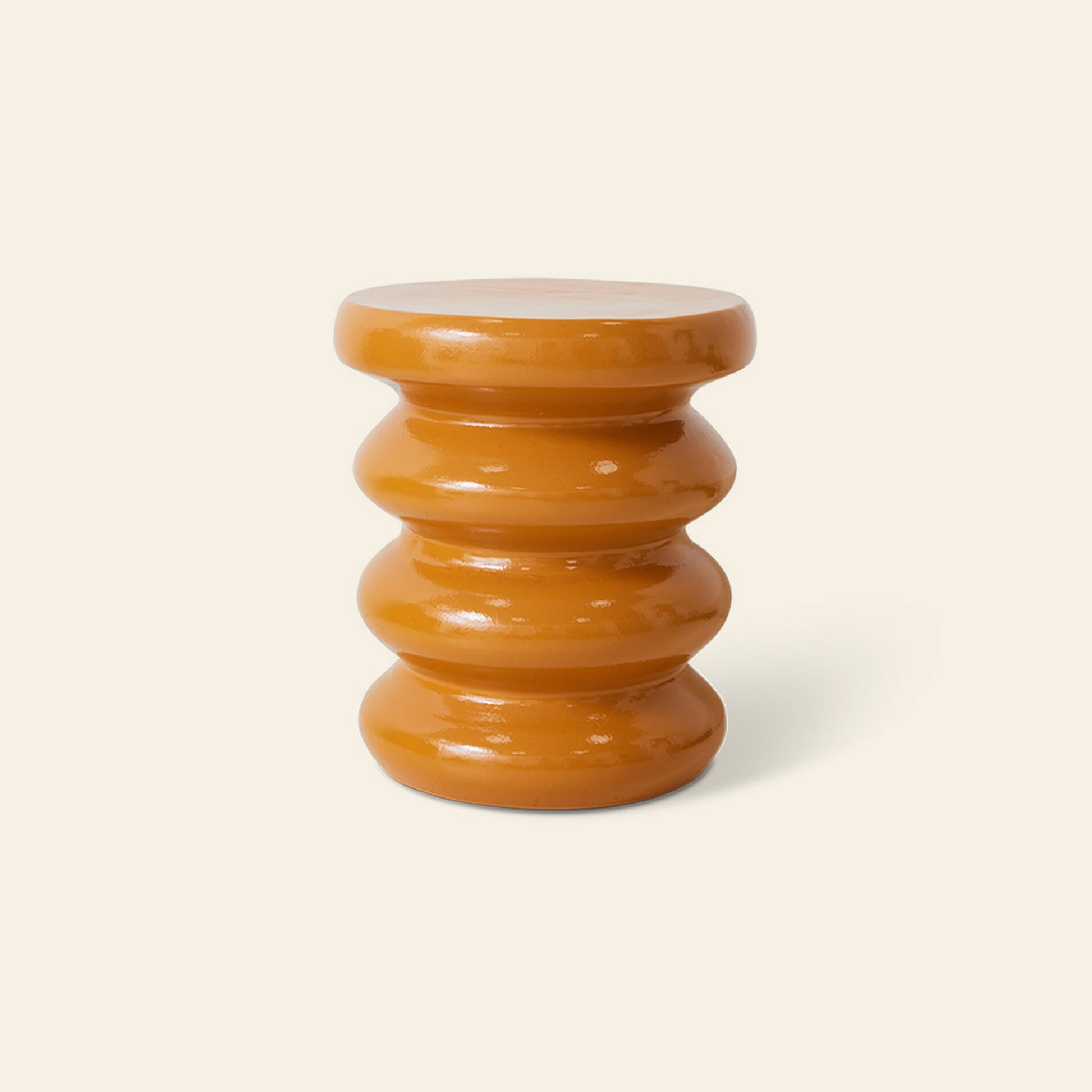 The HKLIVING Allure Side Table by HKLIVING is a glossy, amber-colored ceramic piece with a modern stacked ribbed design and wavy form, set against a plain light beige background.